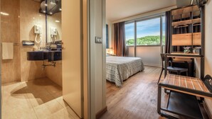 A modern hotel room with a bathroom, a bed, a desk, and a large window with a view. - Hotel Galilei (Pisa)
