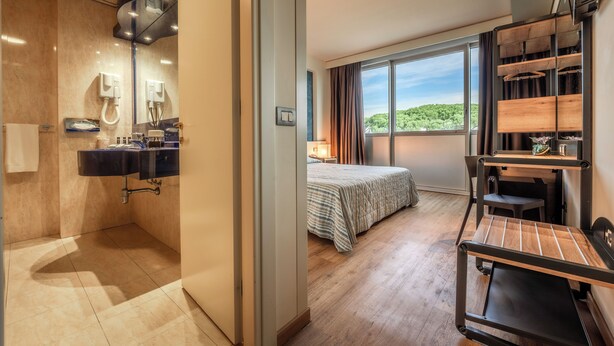 Una habitación de hotel moderna con baño, cama, escritorio y un ventanal con vistas.