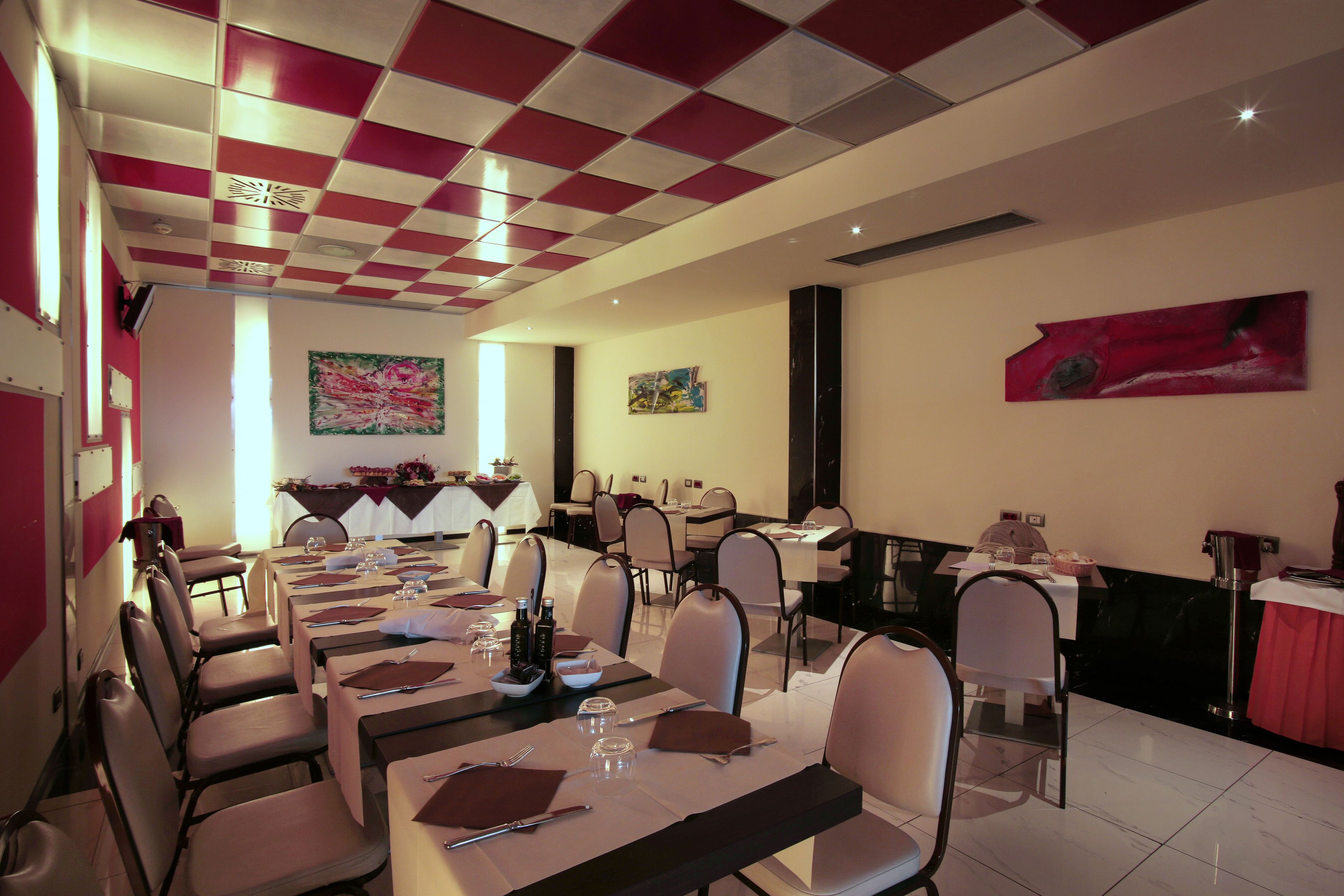 Un comedor con mesas dispuestas para varios comensales, sillas ubicadas a su alrededor y obras de arte en las paredes.