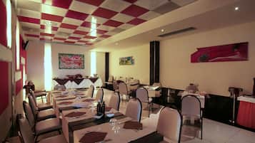 A dining area with tables set for multiple guests, chairs arranged around them, and artwork on the walls.