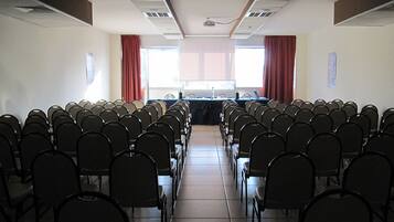 Une salle de conférence avec des rangées de chaises disposées face à une longue table, et un projecteur placé à l’avant.
