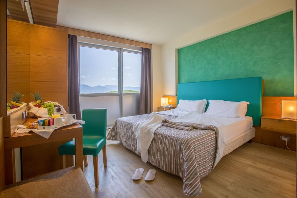 Habitación de hotel con cama, escritorio con desayuno, una silla y vista al exterior.