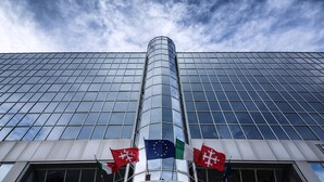 El edificio del Hotel Galilei, con fachada de vidrio moderna y banderas de la Unión Europea, Italia y otro país.