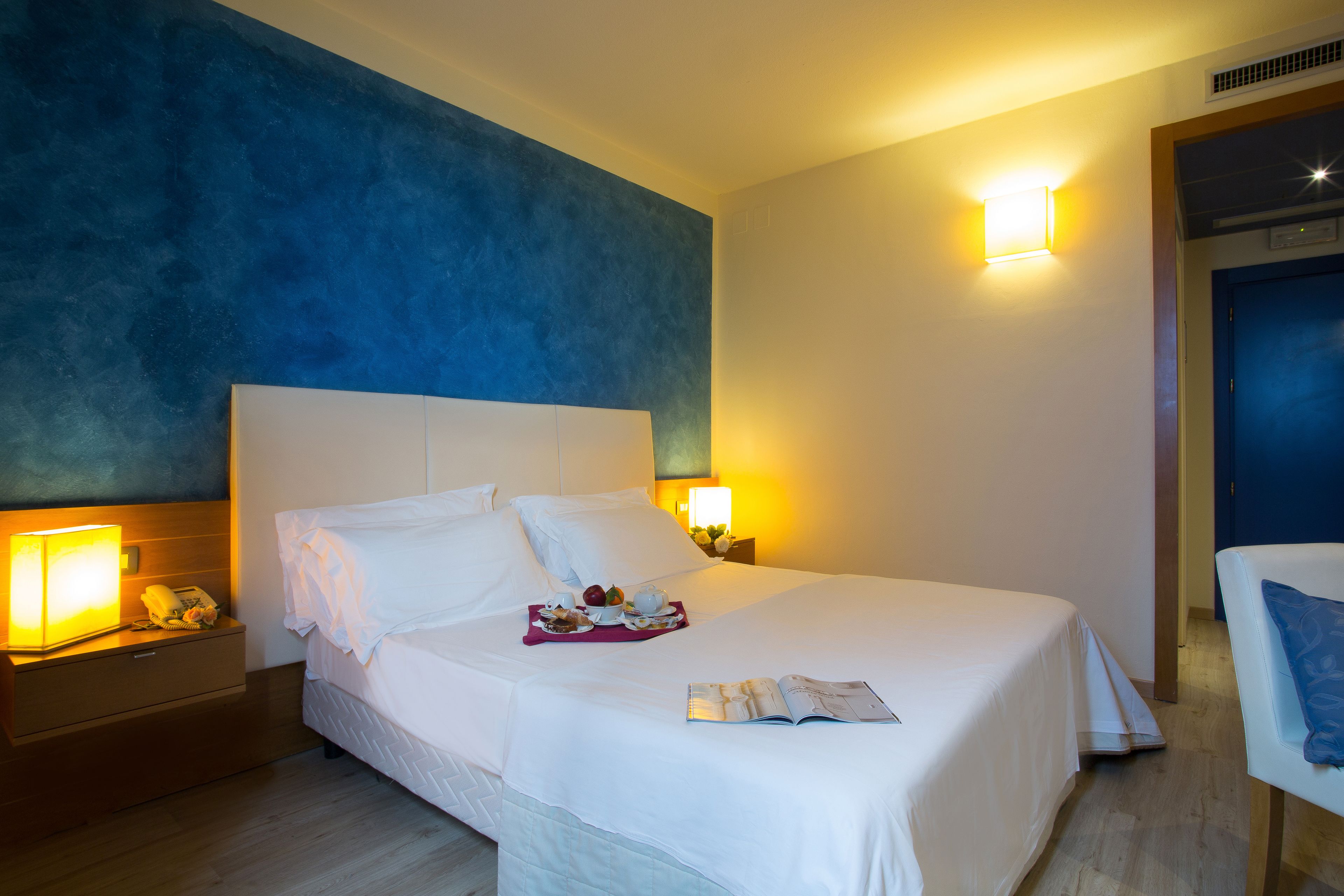 Una habitación de hotel con una cama grande, lámparas de noche, una mesita de noche y una silla.
