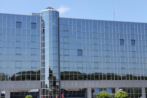 A modern building with a reflective glass facade, a prominent cylindrical structure on the left, and a clear blue sky in the background.