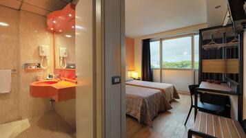 Une chambre d’hôtel avec salle de bain, un lit, un bureau et une vue sur l’extérieur.
