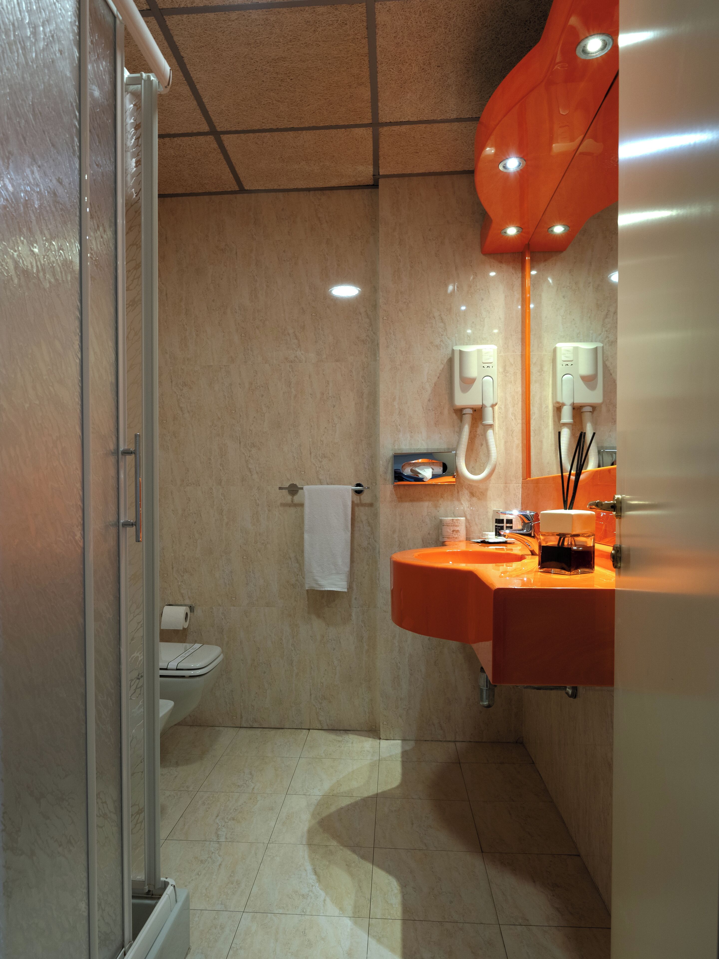 A modern bathroom with a glass shower enclosure, a white toilet, and an orange sink with a mirror above it.