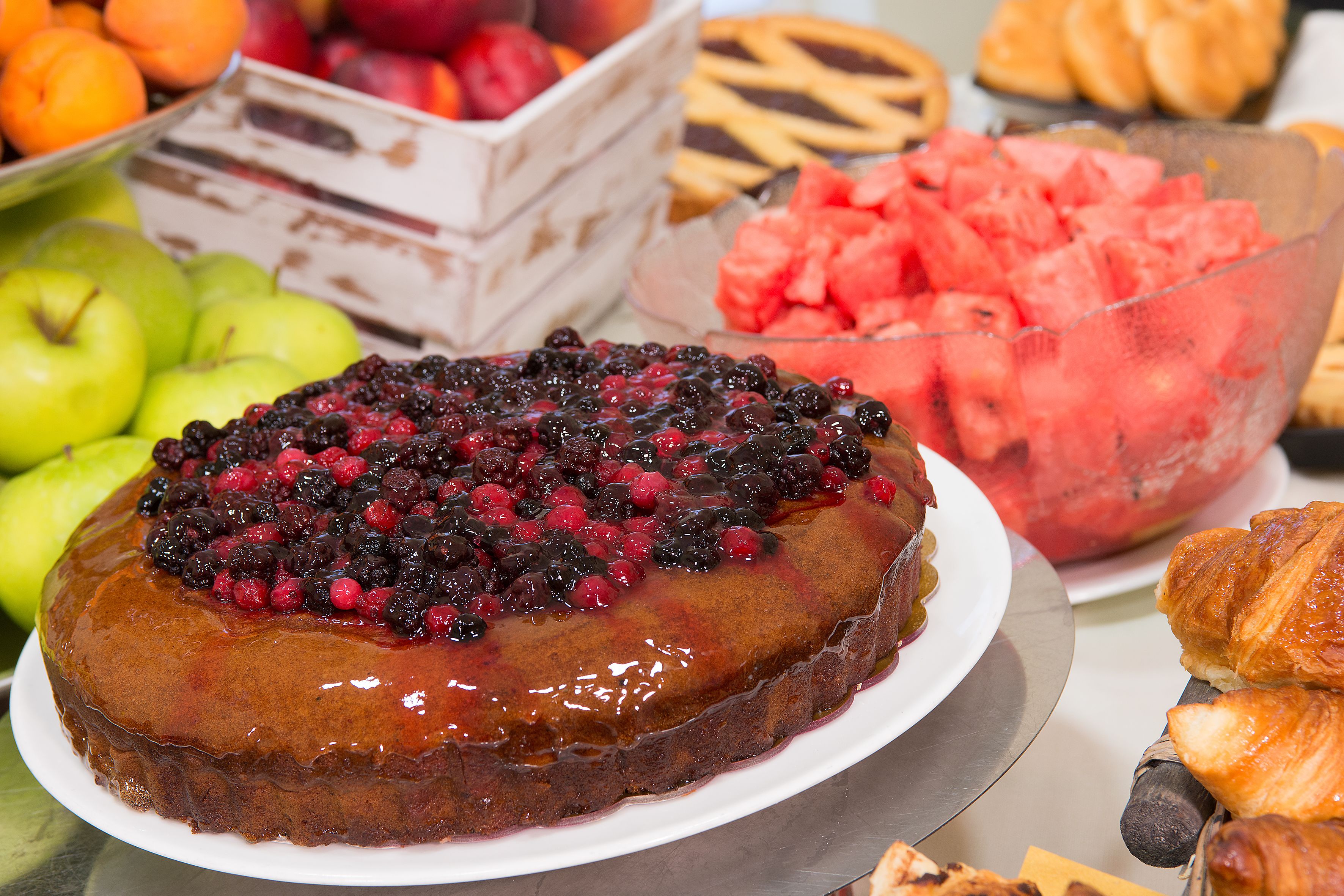 Une table de desserts avec un gâteau décoré de fruits rouges, un saladier de pastèque et un plateau de pâtisseries.