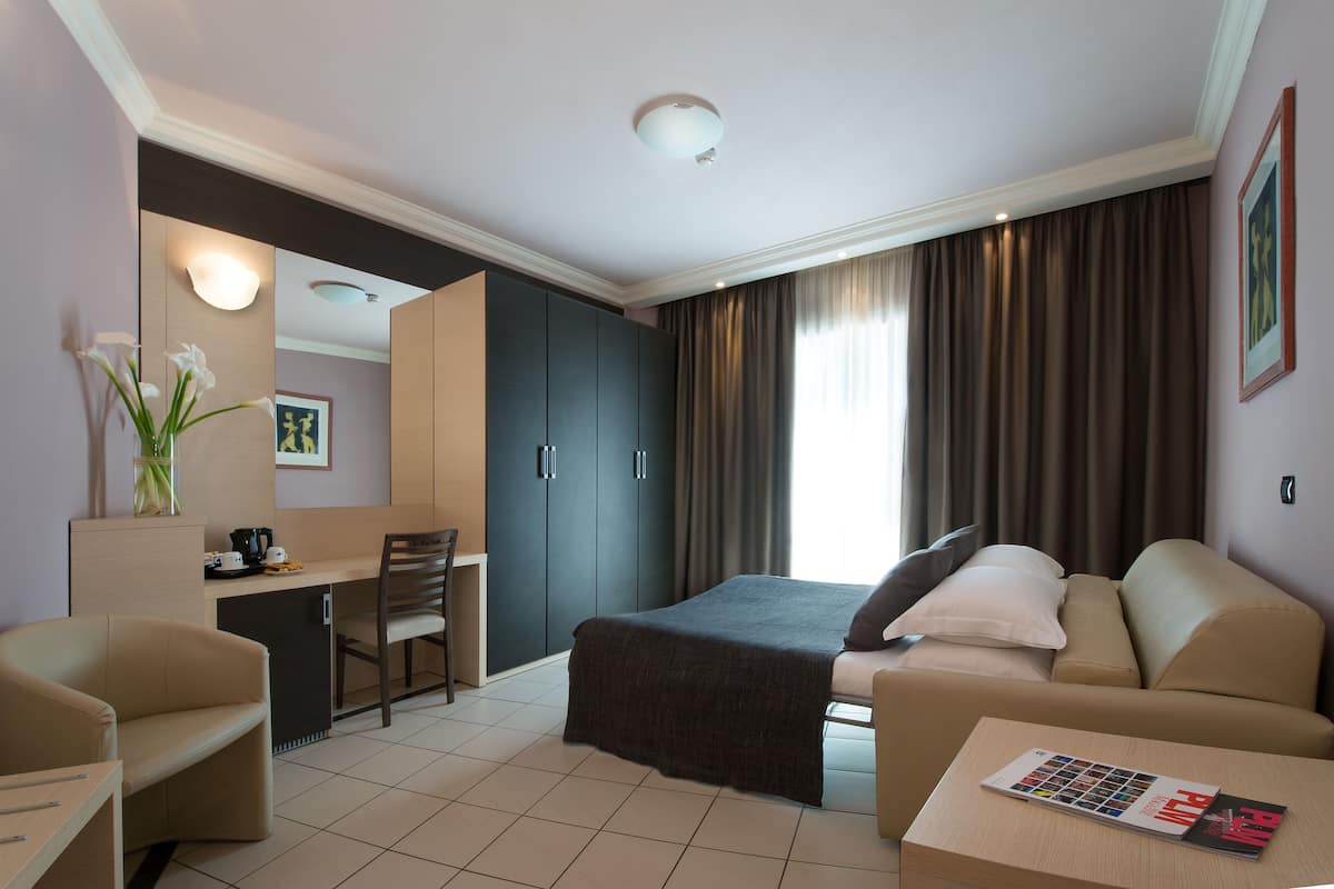 A modern hotel room with a bed, a sofa, a desk, and a chair.