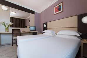 Habitación de hotel con cama, escritorio, silla, televisor y un cuadro en la pared.