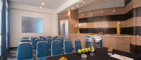 A conference room with blue chairs, a black table with a bowl of fruit, a water bottle, and a projector screen.