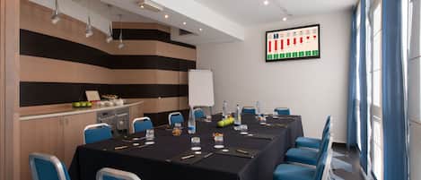 Un salón de conferencias con una mesa larga, sillas azules, una pizarra y un gráfico en la pared.