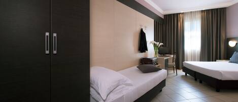 A hotel room with a large wardrobe, two beds, a desk with a chair, and a window with curtains.