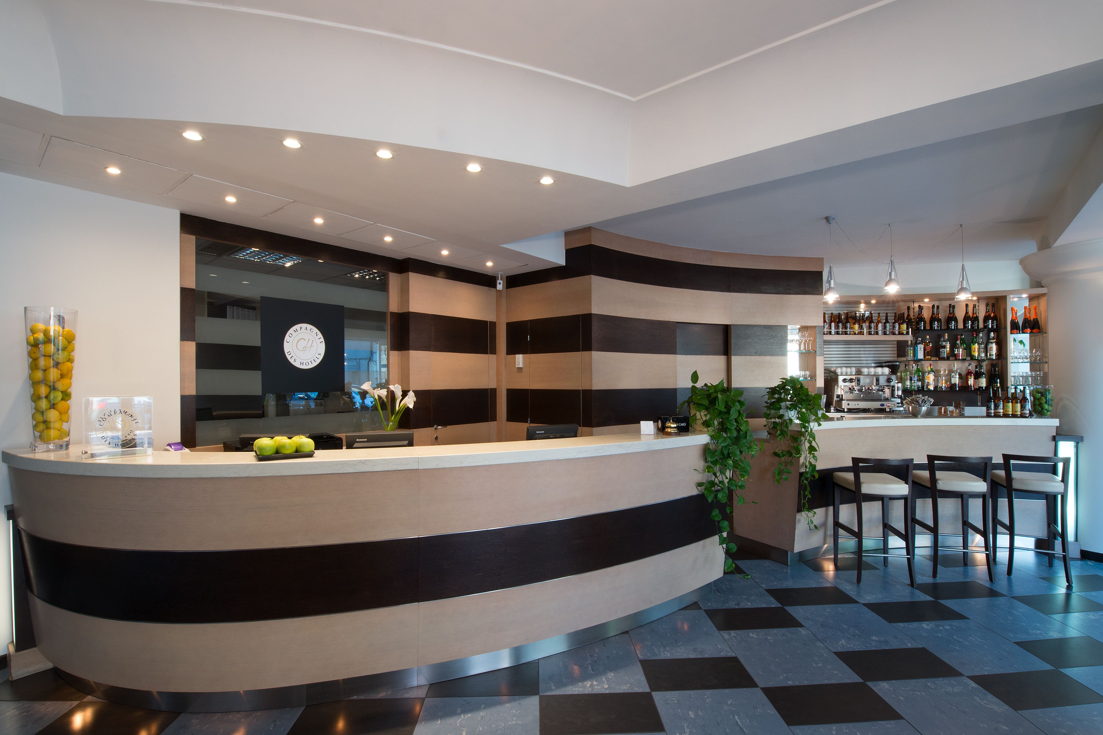 Um hall de hotel moderno com um balcão de recepção curvo, uma área de bar com prateleiras de garrafas e um balcão de check-in.