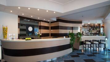 Eine moderne Hotelhalle mit einer gebogenen Rezeption, einer Bar mit Flaschenregalen und einem Check-in-Schalter.