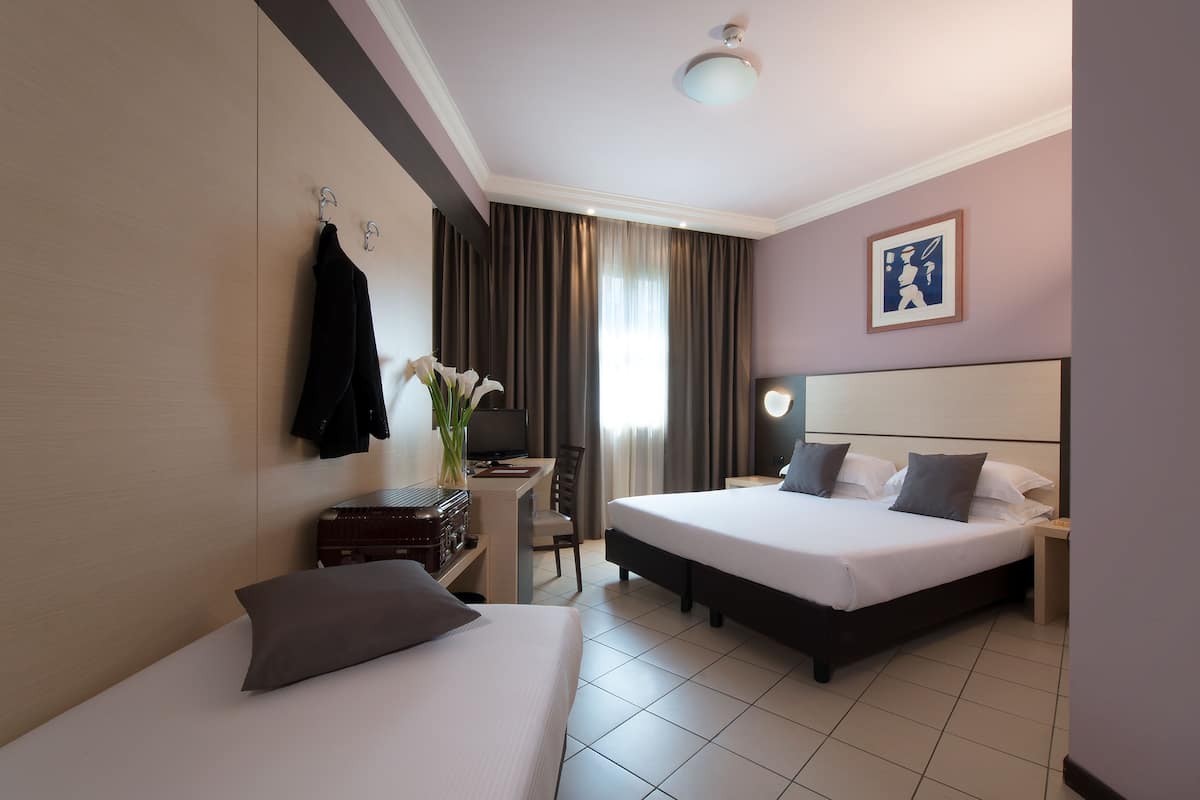 A hotel room with two beds, a desk with a chair, a TV, and a framed picture on the wall.