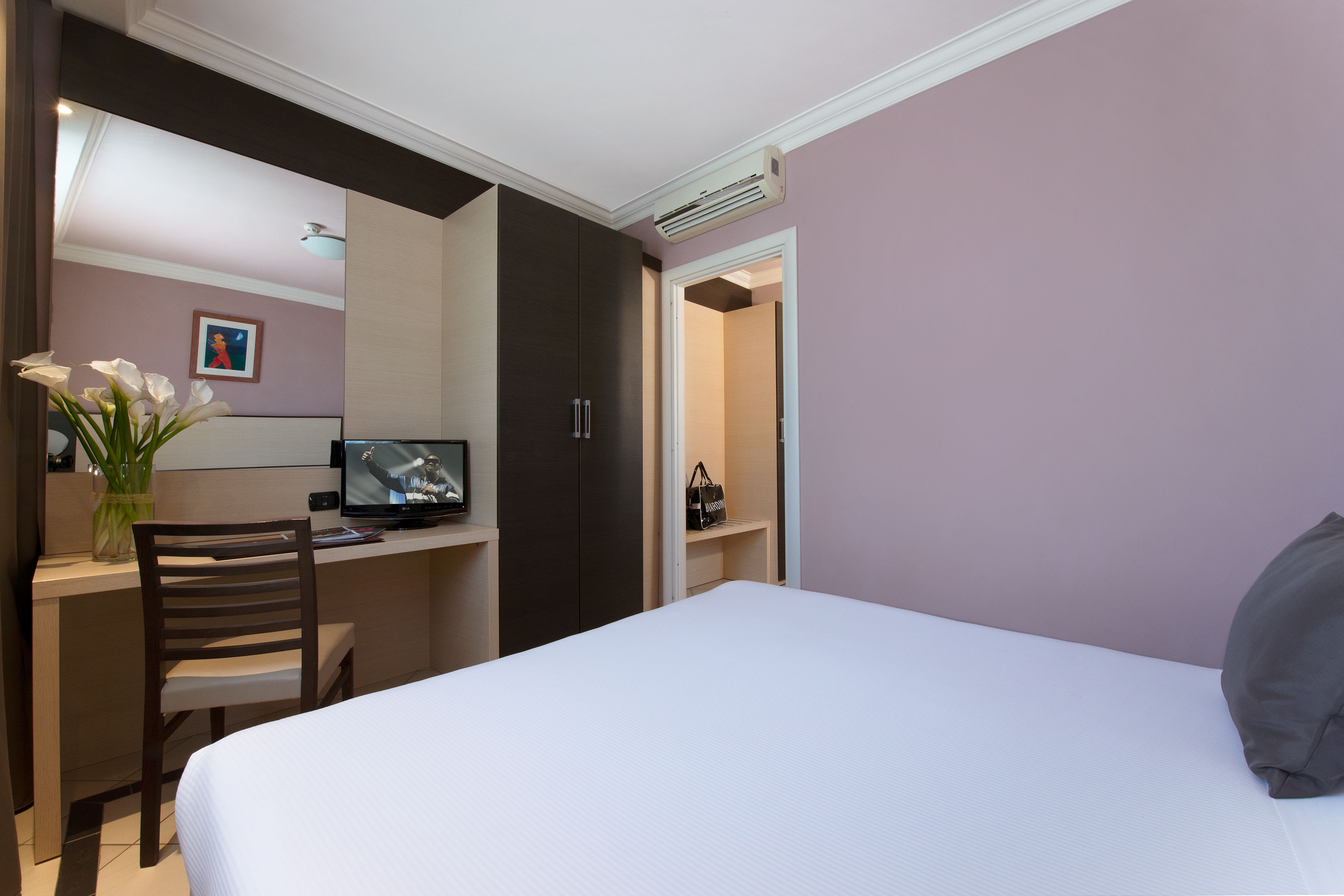 Quarto com cama, escrivaninha, cadeira, televisão e porta do banheiro.