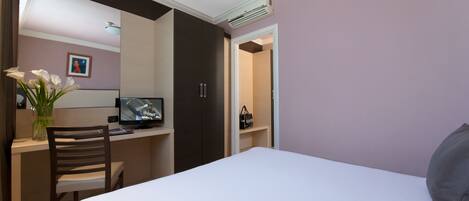 A bedroom with a bed, a desk with a chair, a TV, and a bathroom door.