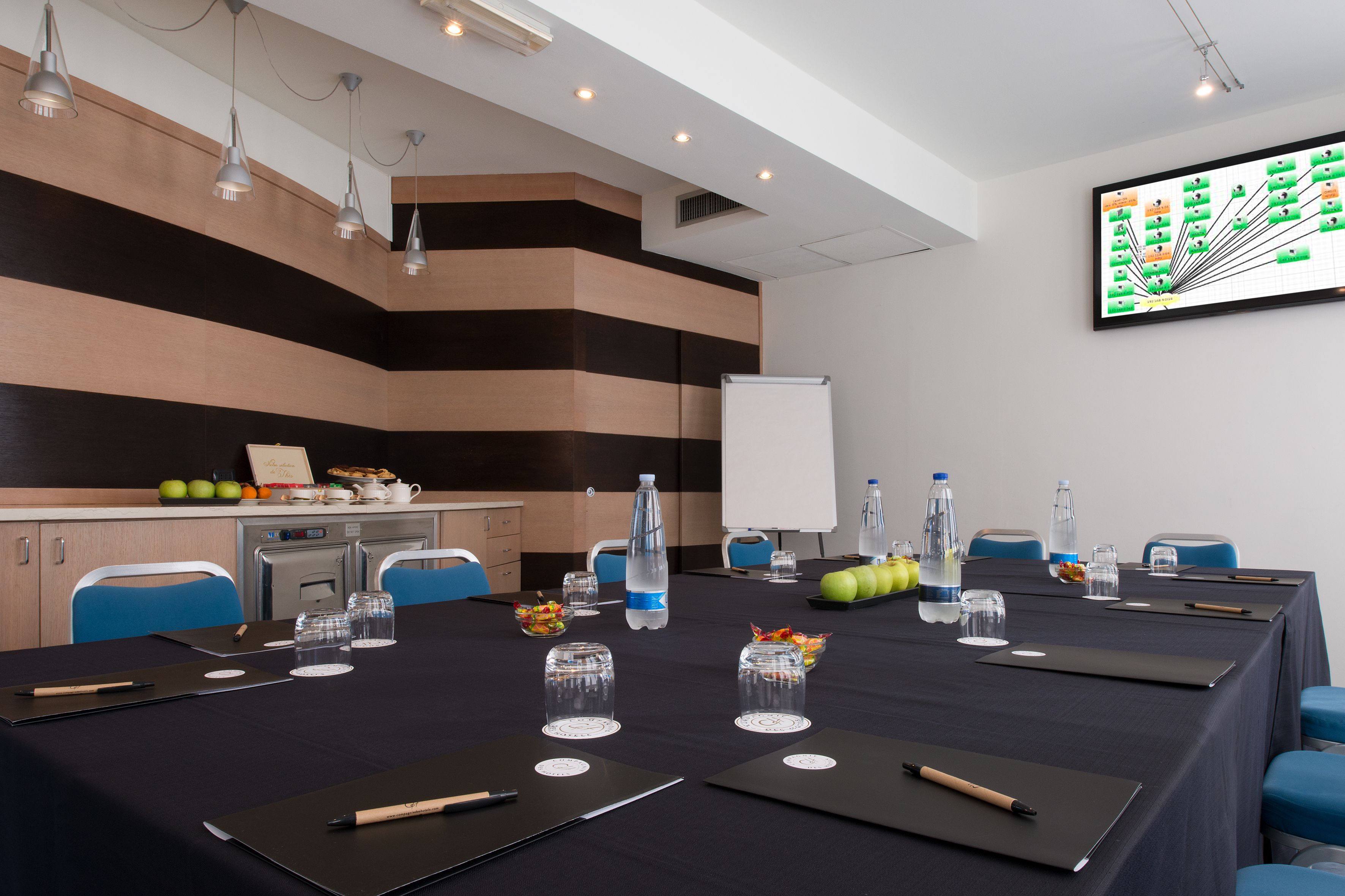 A conference room with a long table, chairs, a whiteboard, and a large screen displaying a chart.