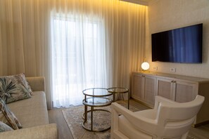 A living room with a sofa, two glass tables, a TV mounted on the wall, and a cabinet.
