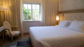 Ein Hotelzimmer mit einem großen Bett, einem Schreibtisch, einem Stuhl, einem Fenster mit Vorhängen und einem Nachttisch mit Lampe.