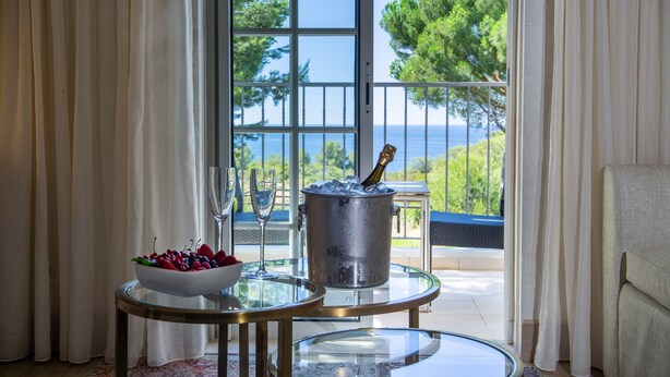 A room with a glass table holding a bowl of fruit and a champagne bottle, a metal bucket, and a view of the sea through a glass door. - Vila Alba Resort (Lagoa)