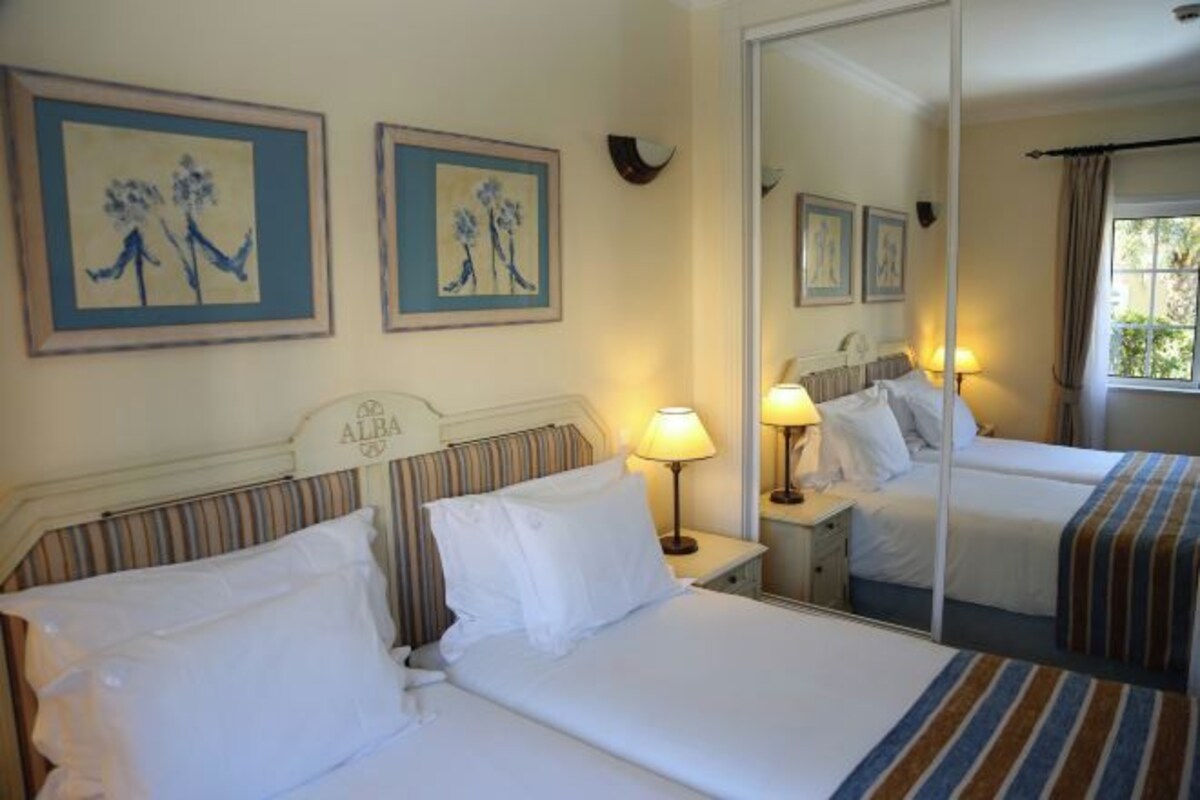A hotel room with two beds, a large mirror, and artwork on the walls.