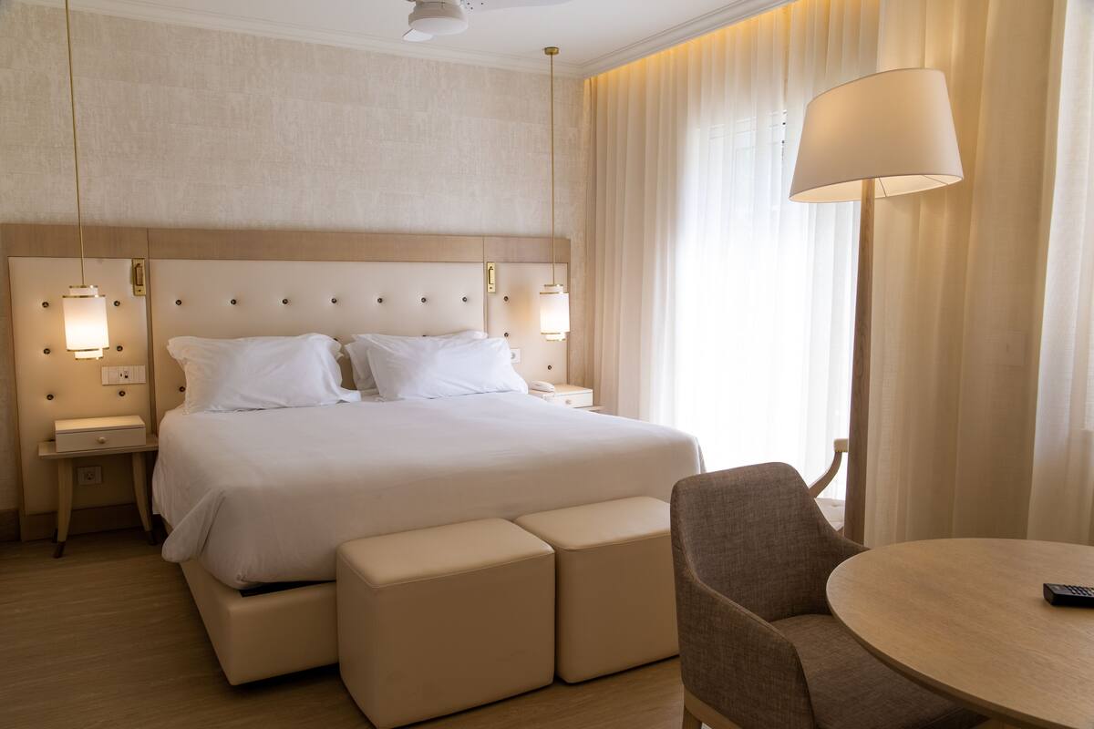 A hotel room with a large bed, bedside lamps, a round table, and a chair.