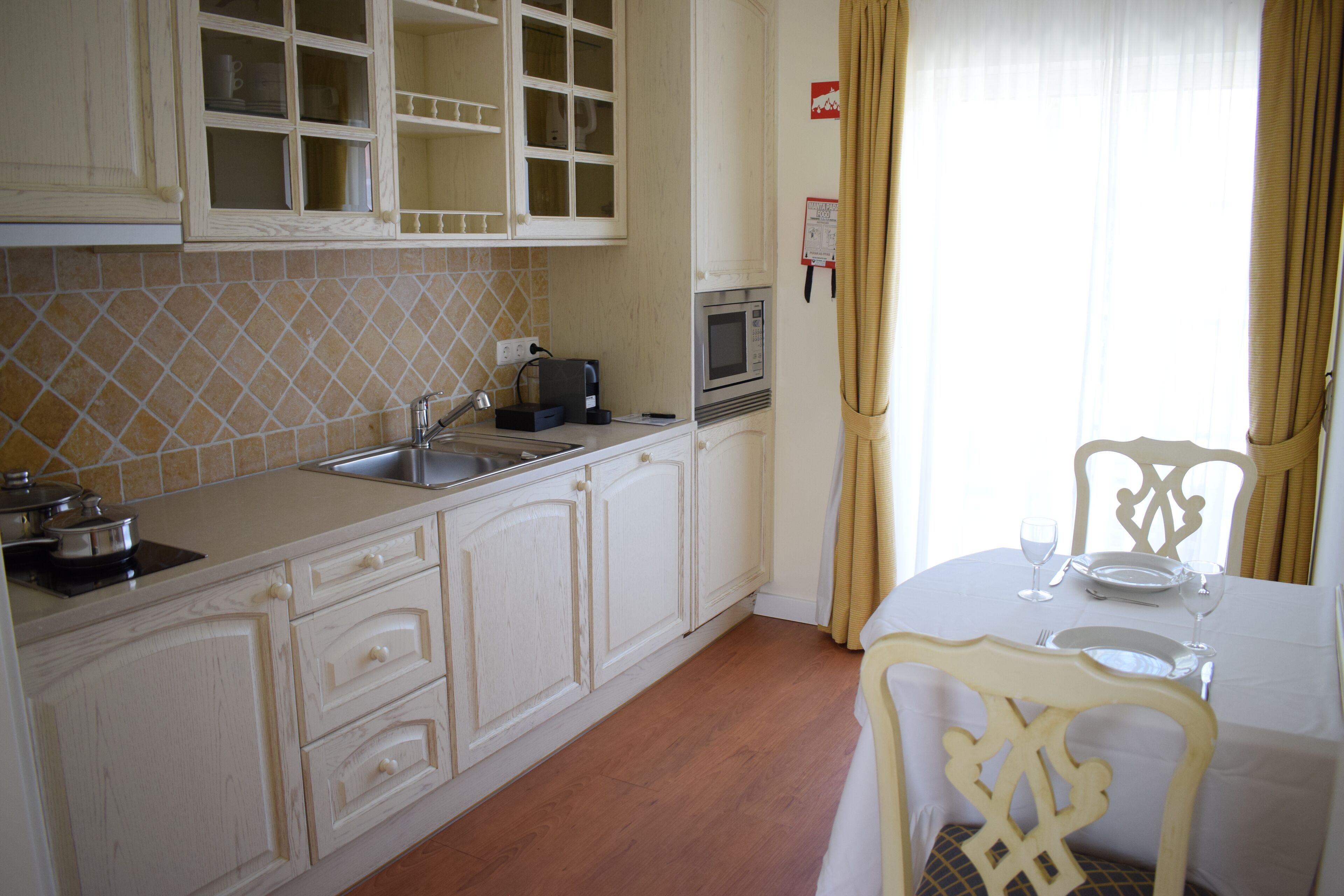 Cocina compacta con microondas, pileta y alacenas. Hay un comedor con una mesa puesta para dos y una silla.
