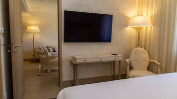 Habitación de hotel con cama, escritorio con lámpara, una silla, televisor en la pared y una puerta que da a otra habitación.