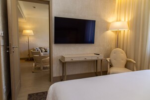 Habitación de hotel con cama, escritorio con lámpara, una silla, televisor en la pared y una puerta que da a otra habitación.