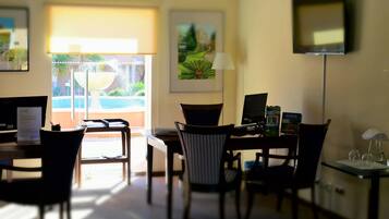 A hotel room with a desk, chairs, a TV, and artwork on the walls.