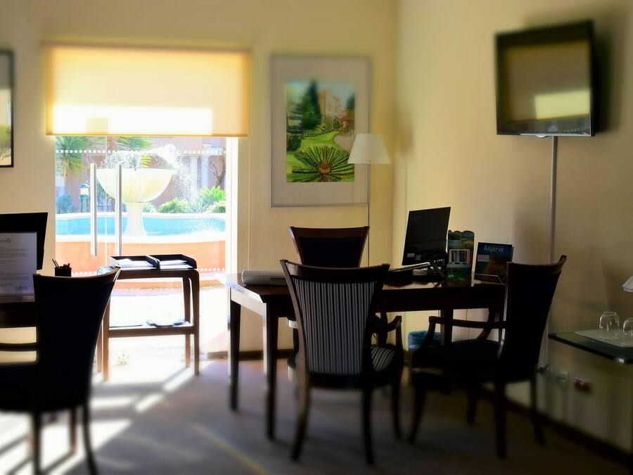 A hotel room with a desk, chairs, a TV, and artwork on the walls.