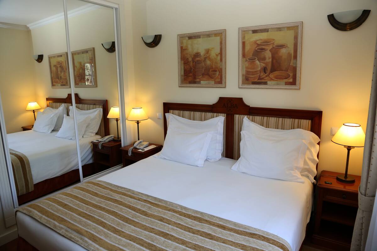 A hotel room with a large bed, two bedside tables with lamps, a mirror, and two framed pictures on the wall.