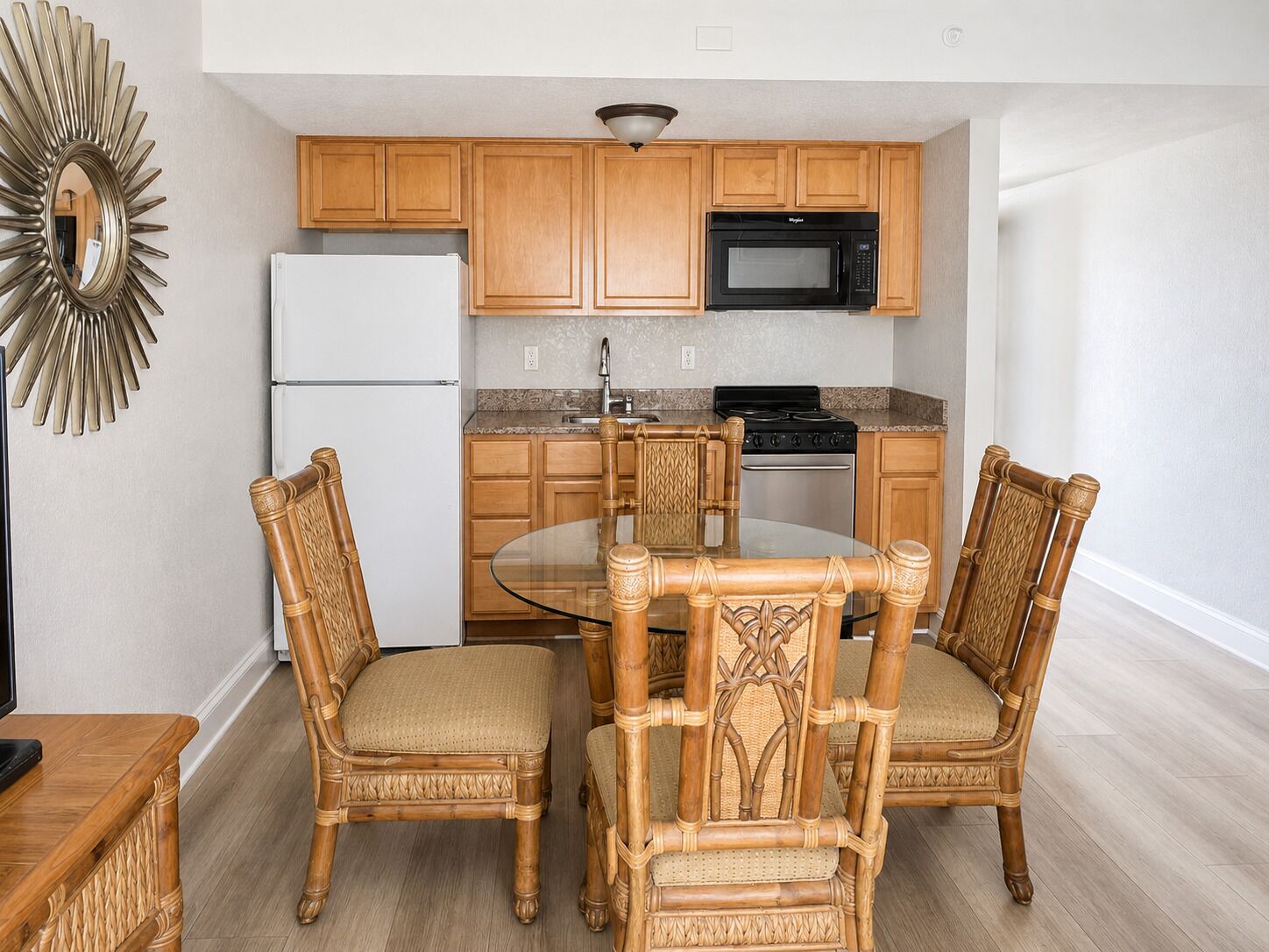 A kitchen with wooden cabinets, a microwave, a stove, and a glass dining table with four chairs.