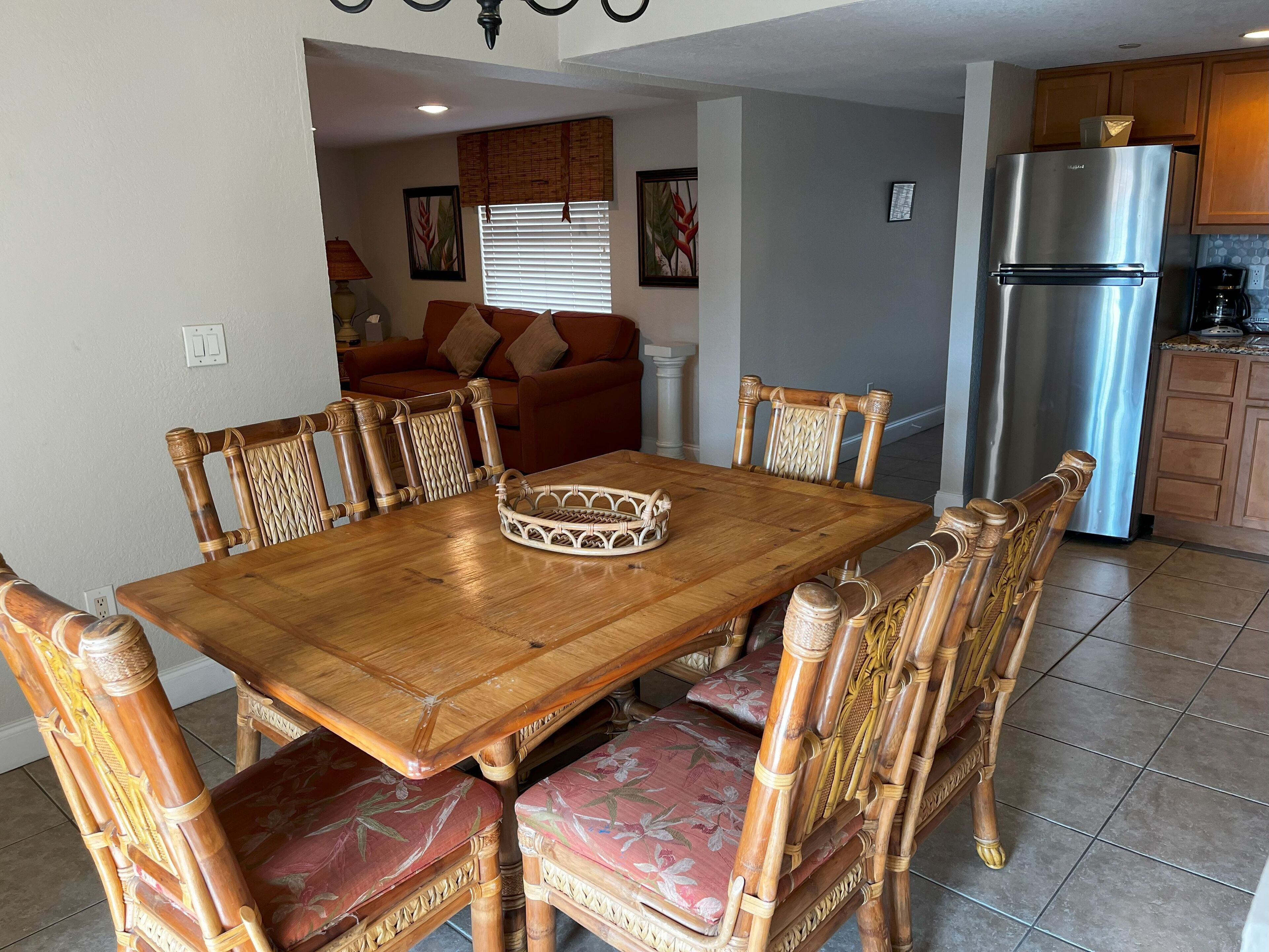 A dining area with a wooden table and chairs, a kitchen with a refrigerator, and a living room with a sofa.