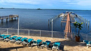 Un port de plaisance doté d’un quai en bois s’étendant dans des eaux calmes, entouré d’une rambarde blanche et de chaises longues bleues.