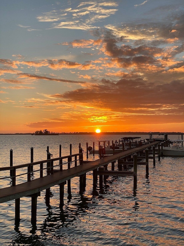 A pier extending into calm water at sunset with the sun low on the horizon.