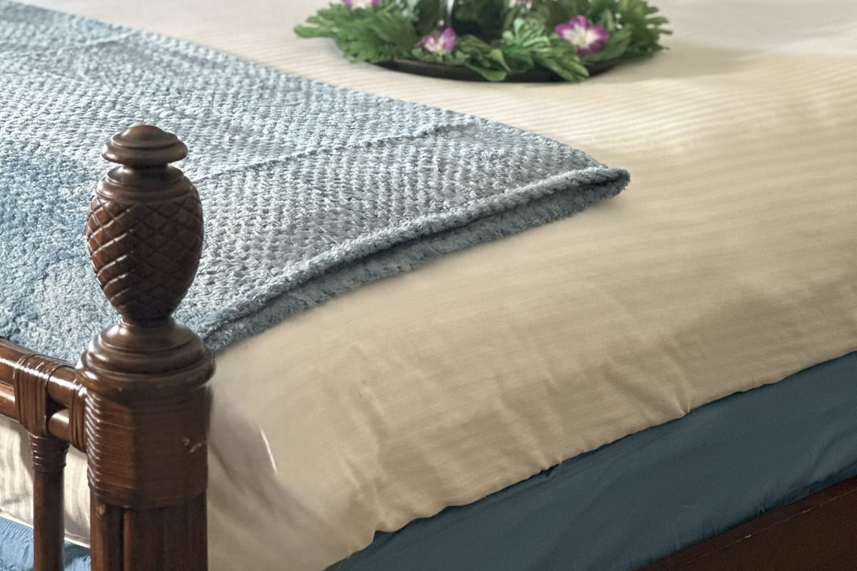 Un lit bien fait, recouvert d’une couvre-lit bleue et blanche, avec deux oreillers, un plateau décoratif sur lequel reposent deux verres de vin rouge, et un plaid bleu.