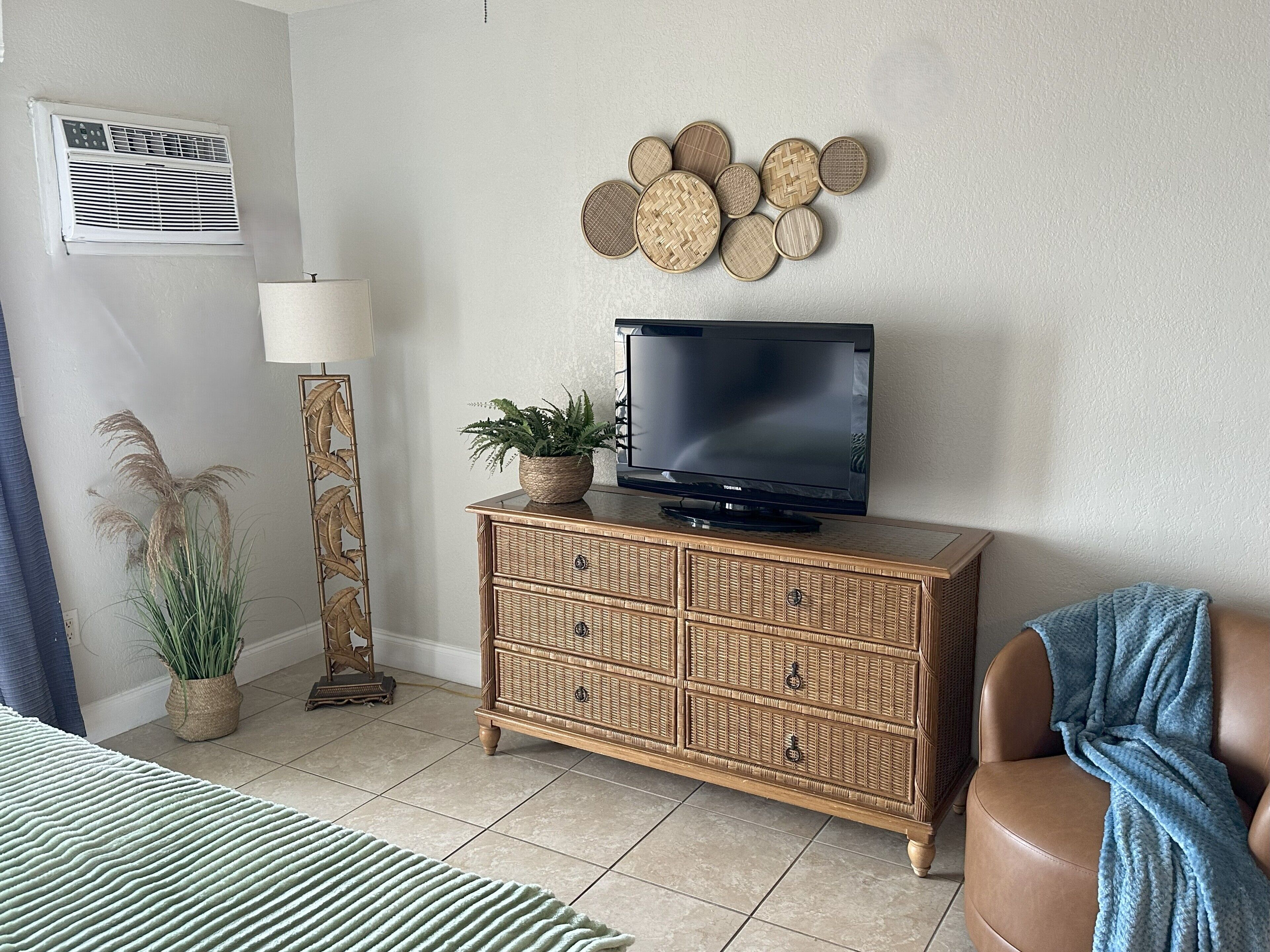 Una sala de estar con un televisor sobre un mueble de madera, una lámpara y una pared decorada con adornos circulares tejidos.
