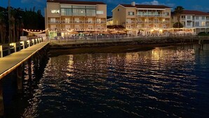 A waterfront hotel with multiple balconies, a dock, and a reflective water surface.