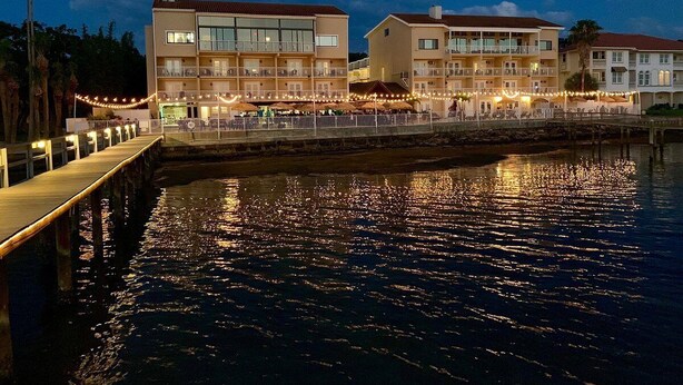 Un hôtel situé au bord de l’eau, doté de nombreux balcons, d’un quai et d’une surface d’eau qui reflète la lumière.