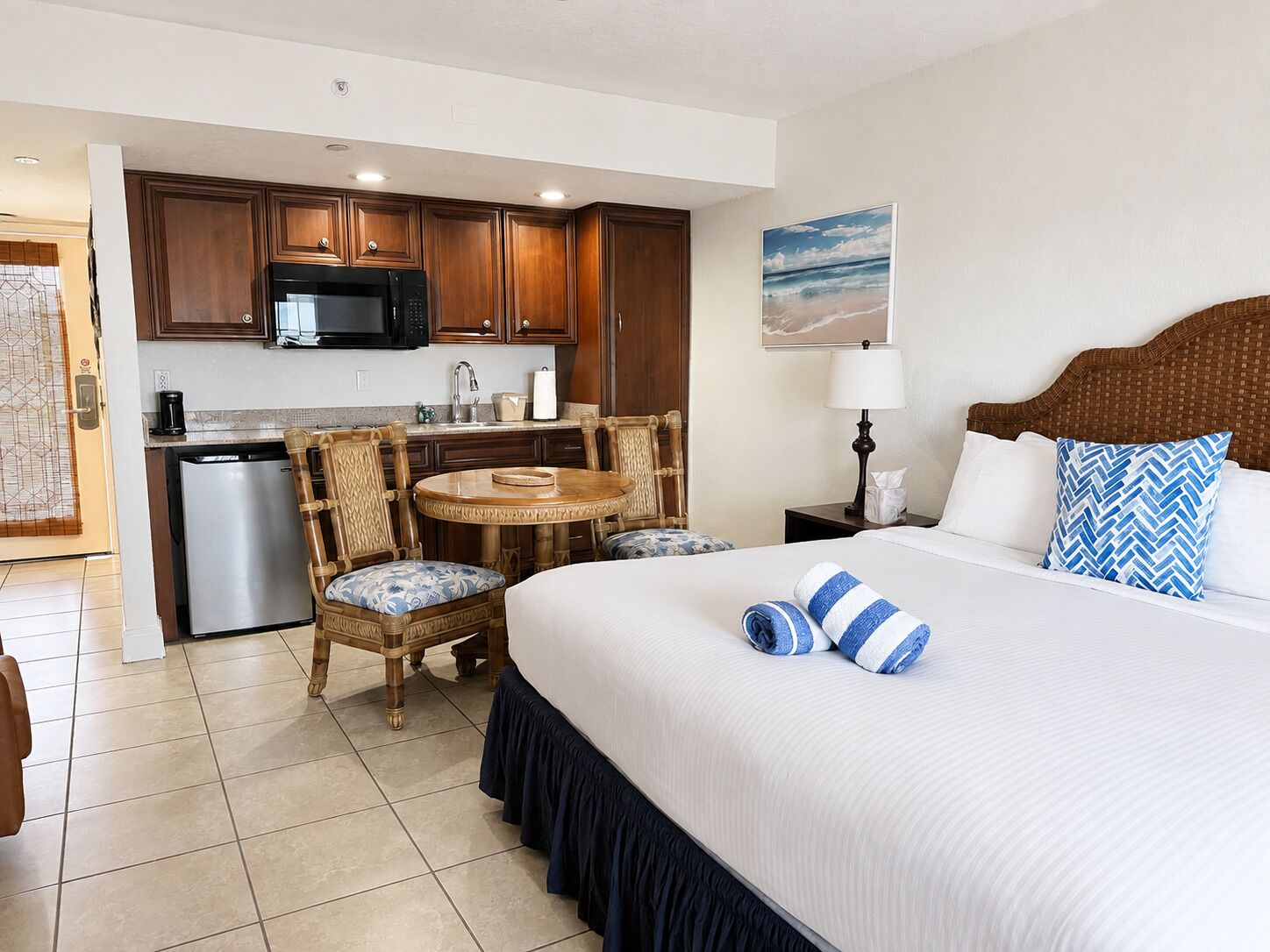 A hotel room with a bed, a dining area with chairs, a microwave, and a refrigerator.