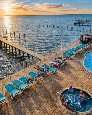 Terraza con sillones reclinables y una bañera de hidromasaje, con vista a una masa de agua y un muelle al fondo.