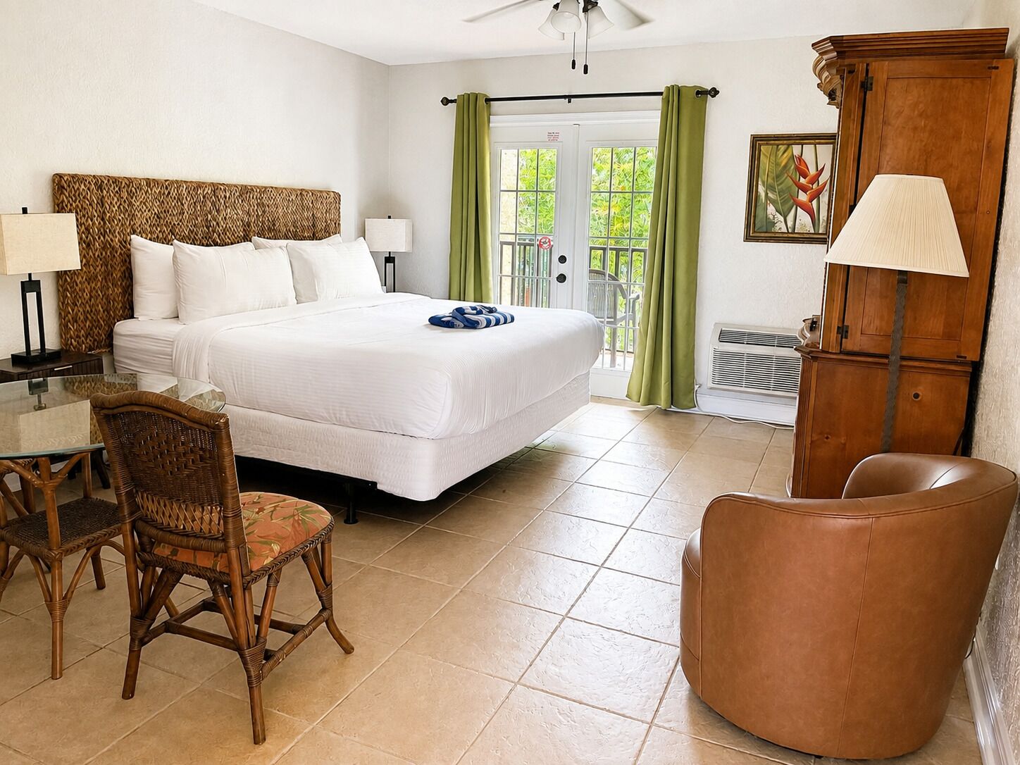 A hotel room with a bed, a chair, a table, a lamp, and a cabinet.