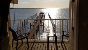 Un balcon donnant sur une jetée qui s’avance dans l’eau, avec deux chaises et une table.