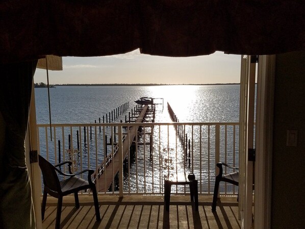 A balcony with a view of a pier extending into the water, two chairs, and a table. - Beso Del Sol Resort (Dunedin)