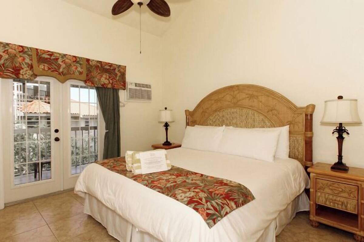 Une chambre d’hôtel avec un lit, une table de chevet, un ventilateur de plafond et une fenêtre donnant sur un beau paysage.