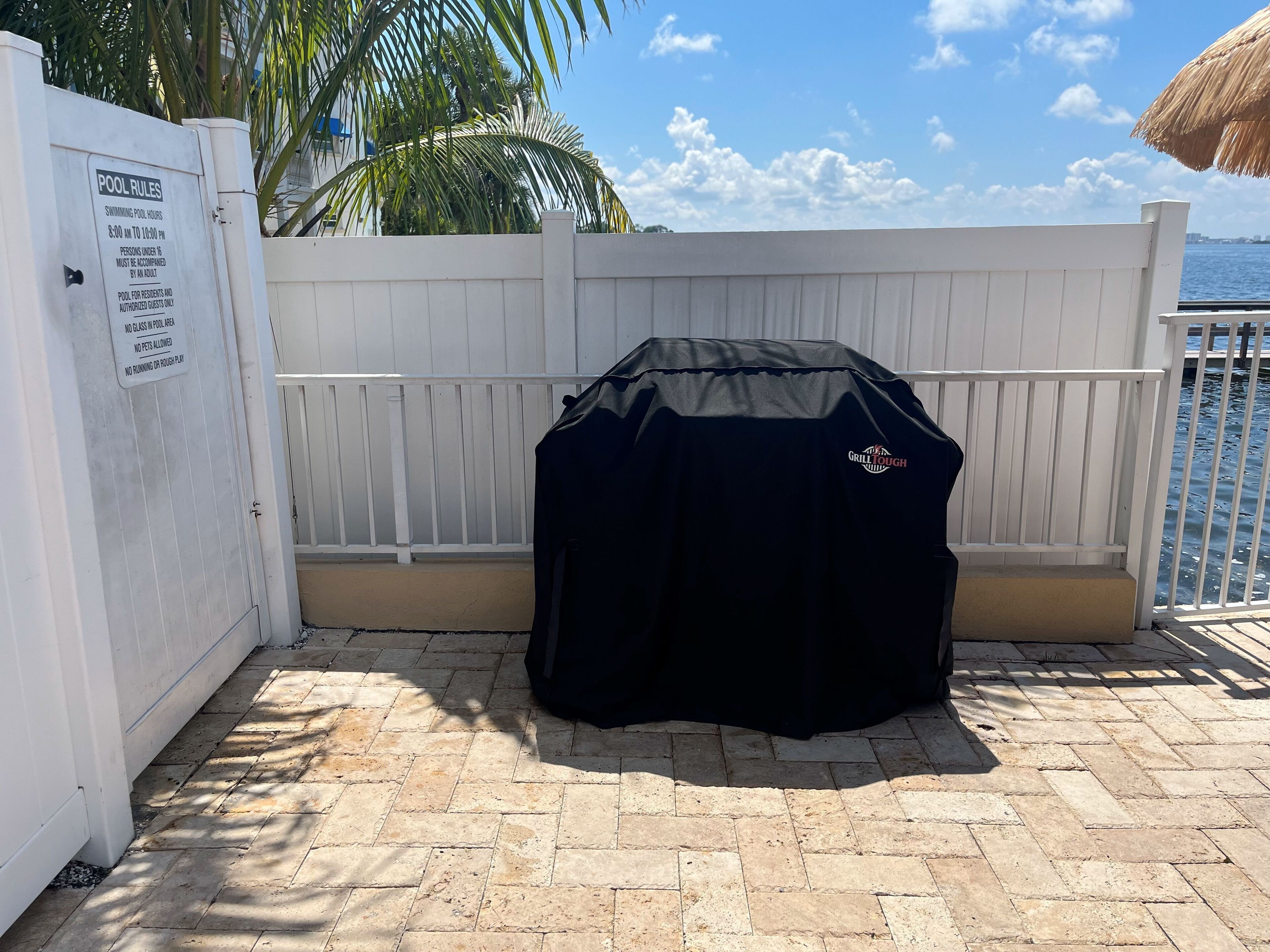 Un barbecue abrité, une clôture blanche et un panneau indiquant les règles à respecter au bord de la piscine.