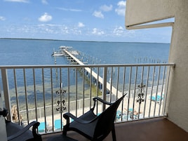 A balcony with a view of a dock and boats, a pool, and lounge chairs.